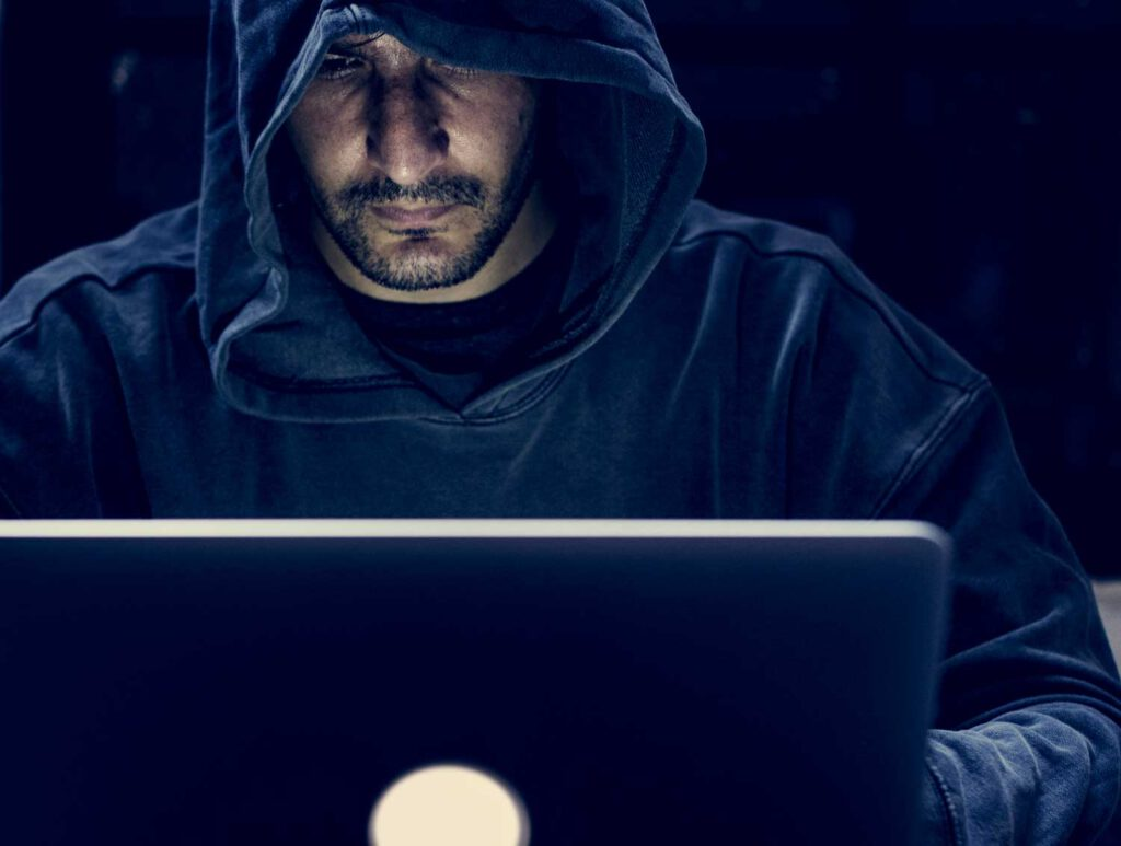Persoon met capuchon achter een laptop — symbool voor cyberdreigingen